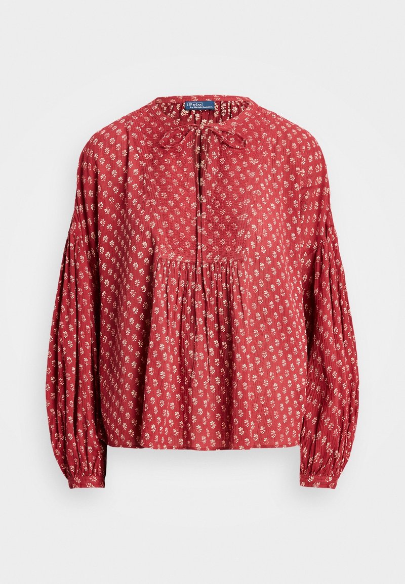 Blouse rouge à manches longues avec petits imprimés floraux blancs, détails plissés et nœud noué au col rond.