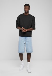 Black oversized t-shirt with short sleeves, paired with light blue denim shorts, and white sneakers. Simple design, no patterns or visible hardware.