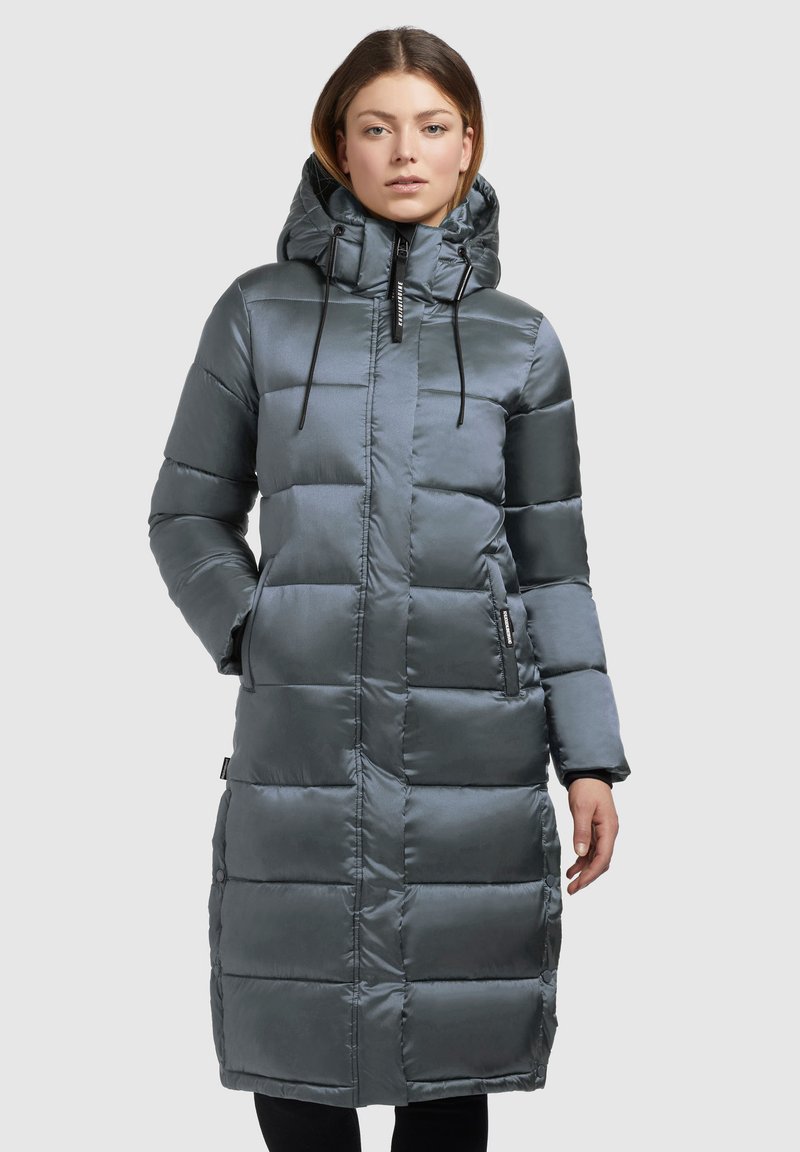 Abrigo largo acolchado en gris oscuro con un acabado brillante, capucha, cordón ajustable, cierre con cremallera y bolsillos laterales. Presenta un diseño acolchado.