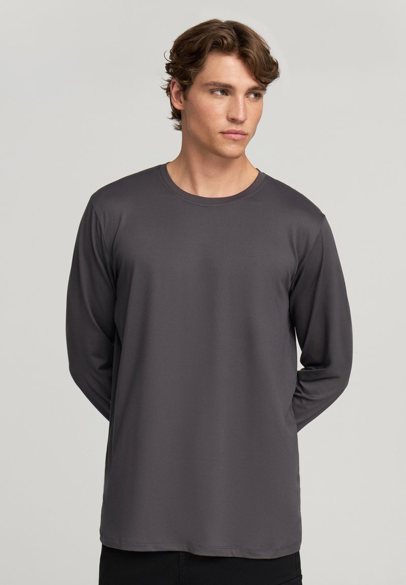 Długi rękaw, koszulka z okrągłym dekoltem w ciemnoszarym kolorze. Wykonana z gładkiego materiału, luźny krój, bez widocznych wzorów czy elementów metalowych.