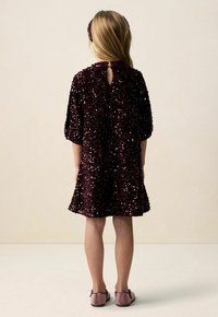 Weinrotes Pailletten-Kleid mit rundem Ausschnitt, kurzen Ärmeln und einem Rückenschlitz. Kombiniert mit passenden rosa Schuhen.