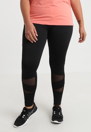 Svarta träningsleggings med genomskinliga paneler, figurnära design och kontrasterande svarta detaljer. Matchas med svarta sportskor.