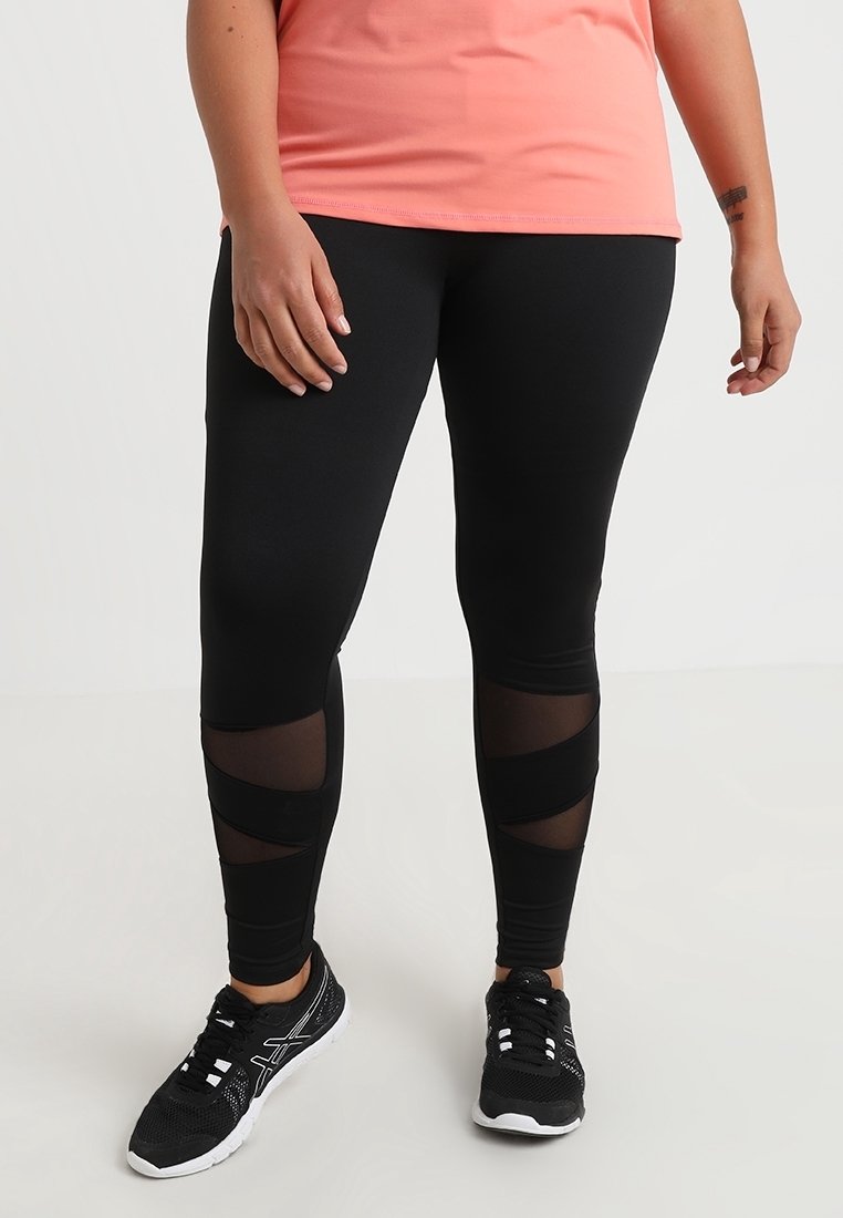 Sorte atletiske leggings med gennemsigtige paneler, tætsiddende design og kontrastfarvet sort trim. Kombineret med sorte sportsko.