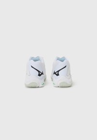 White athletic shoes featuring a textured sole, padded collar, and black logo accents. The design includes a smooth, synthetic upper.