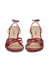 Červené lakované sandále na vysokom podpätku s prackami na členkoch, prekrývajúci sa dizajn, kovové ozdoby a béžová vnútorná stielka s logom "JENNY".