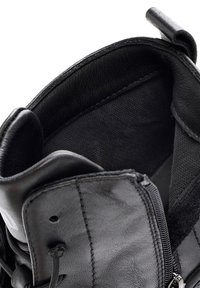 Botte en cuir noir avec œillets, fermeture éclair latérale partiellement ouverte et col rembourré montrant la doublure intérieure.