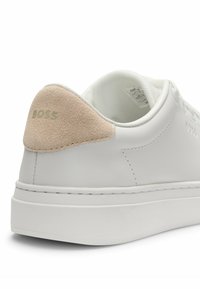 Hvide lædersneakers med en beige ruskindsdetalje på hælen og prægede logo. Tykk gummisål med kontrasterende syninger.