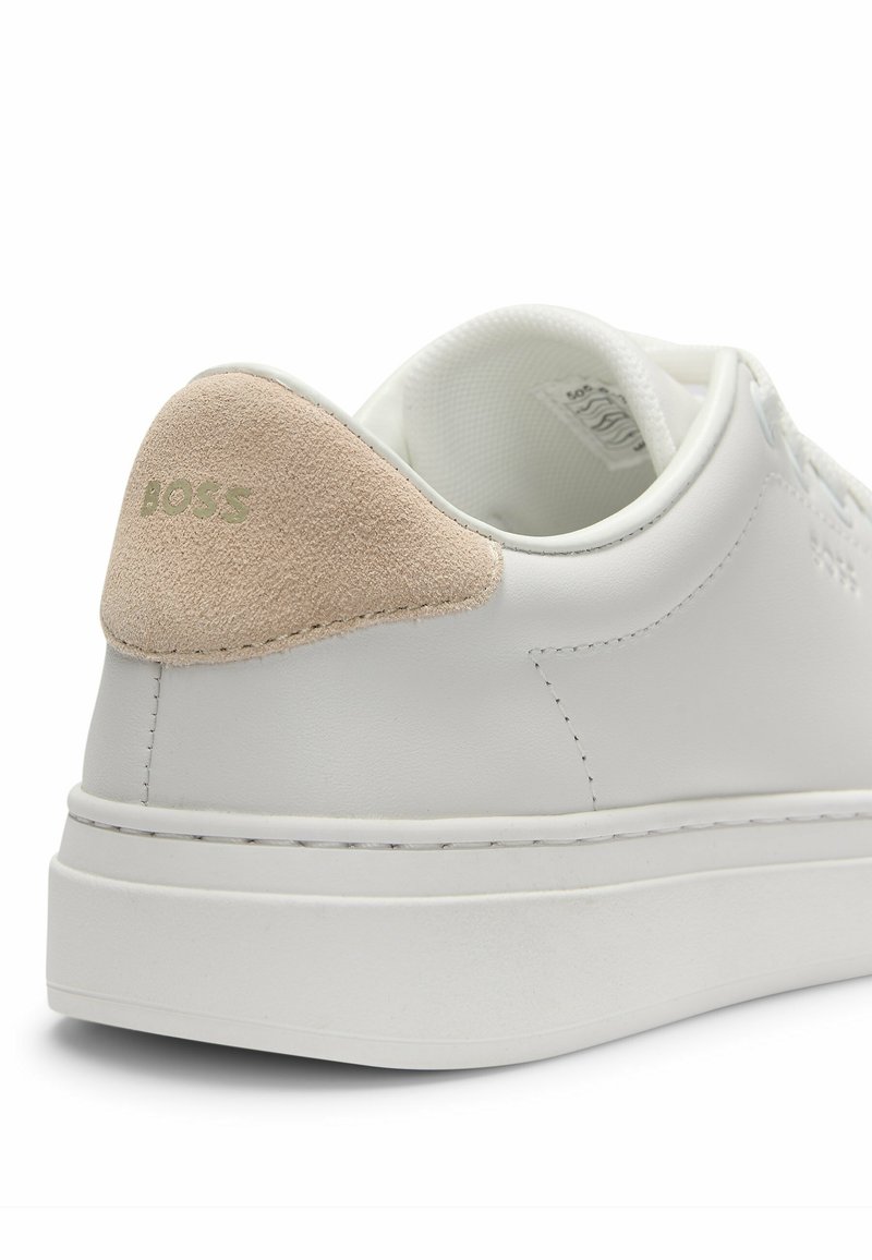 Baskets en cuir blanc avec un accent en daim beige au niveau du talon et un logo en relief. Semelle en caoutchouc épaisse avec des détails de surpiqûre contrastants.