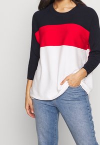 Även en stickad tröja med horisontella block i marinblått, rött och vitt, rund hals och trekvartsärmar. Mjuk textur, avslappnad passform.