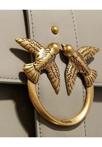 Borsa in pelle grigia con un fermaglio in tonalità oro a forma di due uccelli, con dettagli incisi e un piccolo centro rotondo.