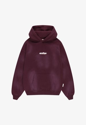 Tume lilla kapuutsiga pusa esiosas tasku ja valge tekst "another" trükitud rinnapiirkonda.