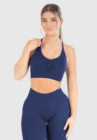 Sujetador deportivo azul marino con detalle fruncido en el frente, tirantes ajustables y un diseño ajustado. Combinado con mallas de talle alto en azul marino.