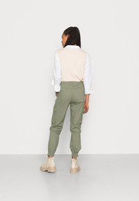 Vaaleanpunainen sleeveless-paita valkoisen paidan päällä, yhdistettynä oliivinvihreisiin cargo-housuihin. Beige taistelukengät täydentävät asun.