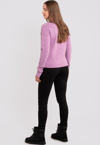 Vaaleanpunainen neulepaita pitkillä hihoilla ja ribbireunalla, yhdistettynä mustiin slim-fit-housuihin ja mustiin nauhakenkiin.