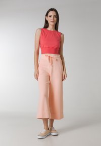 Rød kort tanktop parret med lyse ferskenfarvede vide bukser med elastisk talje og snor. Bæres med beige sneakers.