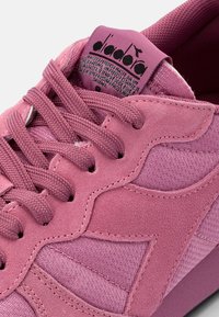 Pink sneaker with mixed materials, including suede and mesh. Features textured surfaces, lace-up design, and a logo label on the tongue.