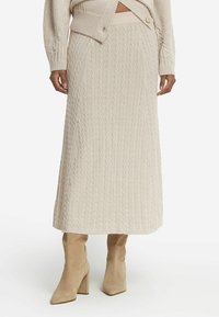 Beige ribbad stickad kjol med vertikala kabelmönster och rak silhuett, kombinerad med beige suède knähöga stövlar.