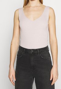 Jasnoróżowy, prążkowany top na ramiączkach z głębokim dekoltem w kształcie V, w połączeniu z czarnymi dżinsami z wysokim stanem. Gładka faktura i dopasowany fason.