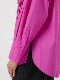 Camisa de manga larga rosa brillante con un corte relajado, que presenta detalles de pliegues y puños con botón. Textura suave y diseño de dobladillo redondeado.
