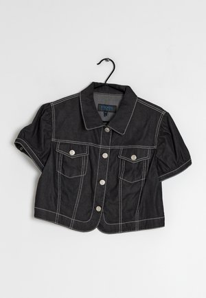 Chaqueta vaquera negra recortada con mangas cortas abullonadas, costuras en contraste blanco, botones plateados, bolsillos con solapa y cuello clásico colgada de una percha.