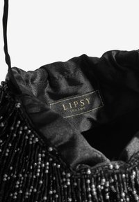 Musta satiininen laukku, jossa on kootut reunat ja helmikuvioitu helminauha. Merkillä lukee "Lipsy London" kullanvärisellä tekstillä mustalla taustalla.