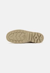Suela de zapatilla de goma beige con surcos profundos, patrones texturizados y ranuras laterales para agarre. Presenta un logotipo en forma de diamante en la entresuela.