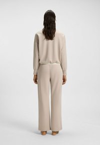 Beige loungepak met een loszittende pullover met lange mouwen en hoge taille wijde broek, gemaakt van een gladde, zachte stof.