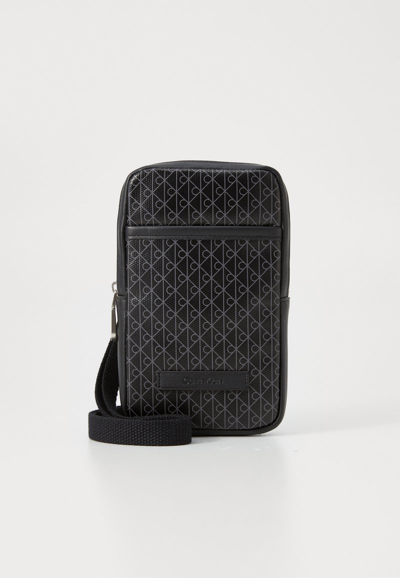 Geantă de umăr neagră cu un model geometric, fabricată din material texturat. Dispune de o curea ajustabilă și un buzunar frontal cu fermoar, decorat cu un logo.