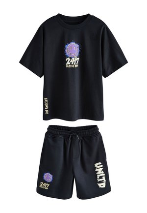 Dreng iført sort T-shirt og shorts med smilende ansigt og teksten "24/7 State of Mind", stående mod en ensfarvet beige baggrund.