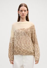 Chunky strikkegenser i en gradient fra krem til lys brun. Har rund hals og lange ermer med strukturert overflate.