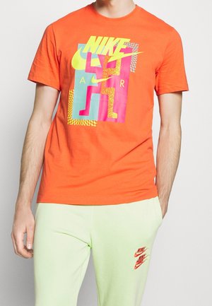 Orange Nike T-Shirt mit grafischem Design in hellen Farben, einschließlich pinken und neongrünen Elementen, in einer Standardpassform.