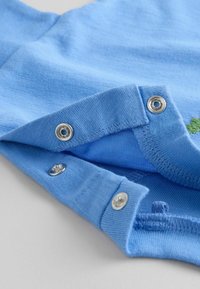 Gros plan sur un tissu bleu avec trois boutons-pression métalliques partiellement attachés, montrant les détails de couture sur un matériau textile doux.