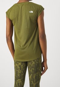 Olivgrön ärmlös tröja med rundad halsringning, med en liten vit logotyp på baksidan. Matcher med mönstrade gröna leggings.