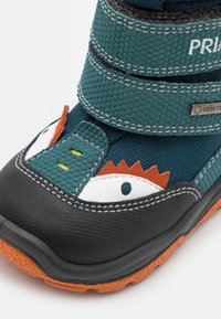 Barnestøvler med en strukturet teal-overdel, sort gummisål og orange accenter. Inkluderer borrelåse og legende øjen-designs.