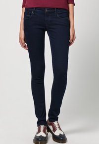 Jeans ajustados en denim azul marino oscuro, con una textura suave, diseño clásico de cinco bolsillos y cierre de botón en tono cobre.