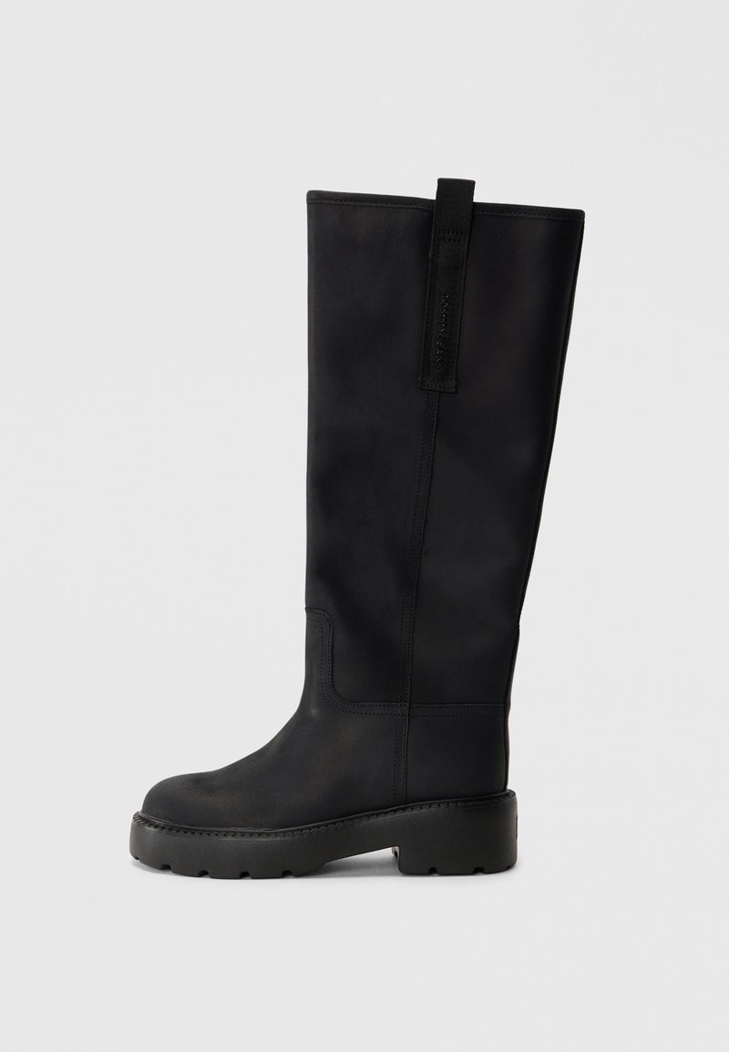 Black knee-high boots made of smooth leather, featuring a rounded toe, thick sole with treads, and a pull tab at the back.