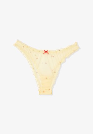 Tanga de color amarillo pálido translúcido con pequeños estampados de frutas, bordes con volantes y un pequeño lazo rojo en el centro de la cinturilla frontal.