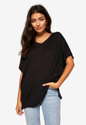 T-shirt nera a V, realizzata in tessuto morbido, vestibilità ampia, maniche corte, con tasca laterale, abbinata a jeans azzurri chiari.