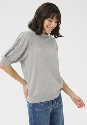 Pull en tricot gris clair avec un col haut, des manches courtes bouffantes et un ourlet côtelé. Associé à un jean droit bleu foncé.