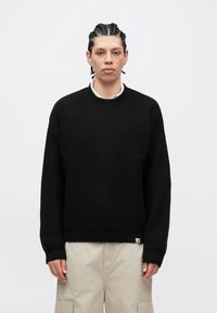 Pulover negru tricotat cu un model texturat în carouri, cu decolteu rotund și manșete plisate. Etichetă mică cu logo la tiv.