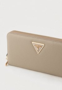 Bézs bőr pénztárca texturált felülettel, aranyszínű fémrészletekkel és háromszög alakú logó díszítéssel. Felül cipzáras zárral rendelkezik.