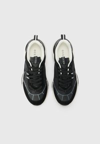 Black sneakers with a textured upper, white interior, and reflective accents. Features laces and a rubber sole with grey geometric patterns.
