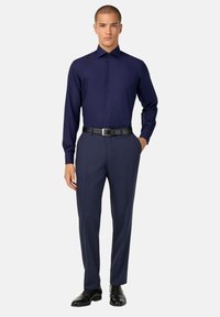 Marineblaues Langarmhemd mit einem knopfbaren Design, kombiniert mit strukturierten Hosen und einem schwarzen Gürtel, abgerundet mit polierten schwarzen Schuhen.