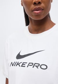 Κοντινό πλάνο ενός ατόμου που φοράει λευκό t-shirt Nike Pro με μαύρο λογότυπο Swoosh στο στήθος.