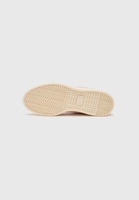 Semelle de chaussure en caoutchouc avec un motif zigzag texturé, de couleur beige. Bords lisses et accent rectangulaire dans la zone de la semelle intermédiaire.