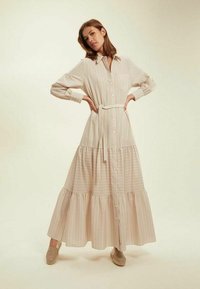 Robe chemise rayée à manches longues en crème et couleurs pastel. Comprend un devant à boutons, une ceinture à la taille et un ourlet volanté en étages.