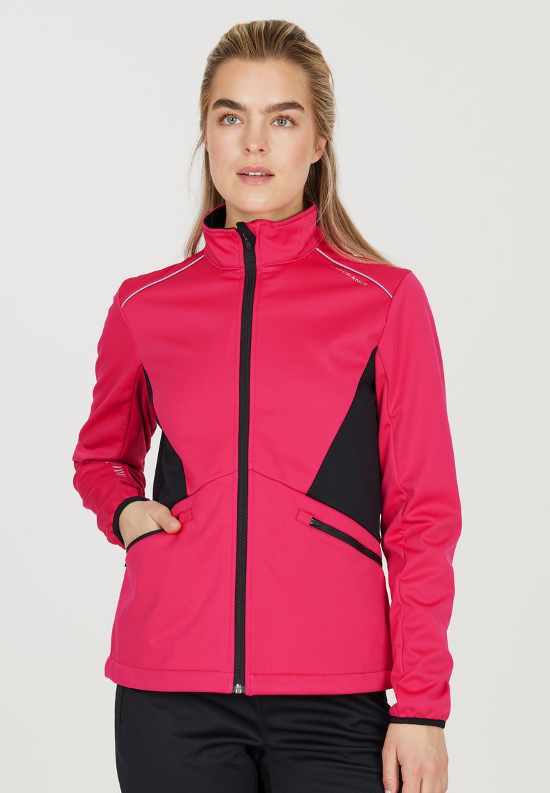 Veste ajustée en rose vif avec des accents noirs, col montant, zip intégral et deux poches latérales. Comprend des détails réfléchissants sur les épaules.