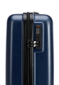 Valigia rigida blu navy con finitura testurizzata, doppie cerniere, lucchetto a combinazione e tirazips con logo. Forma compatta e rettangolare.