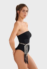 Svart strapless baddräkt med en åtsittande overdel och en midjerem med ett vitt abstrakt mönster. Slät tygkvalitet, högskuren ben-design.