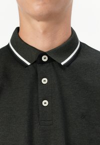 Tume roheline polo särk, millel on tekstuurne kangas, valge triibuline krae ja kolm nööpi heledate nööpidega.